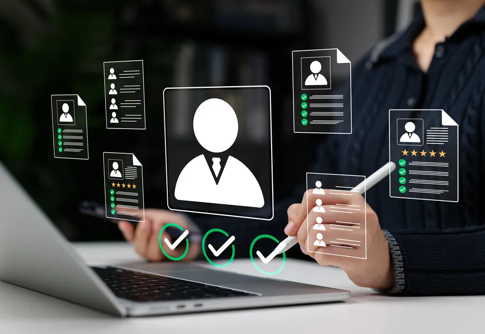 Person at a laptop reviewing digital candidate profiles with verification checkmarks